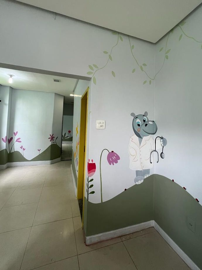 Corredor de acesso aos consultórios, com mural de flores e um hipopótamo de jaleco e estetoscópio pintado na parede
