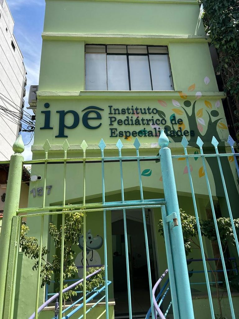 Fachada verde da Clínica IPÊ no número 157 da Rua Delfim Moreira, com o letreiro do Instituto Pediátrico de Especialidades e folhas coloridas pintadas na parede
